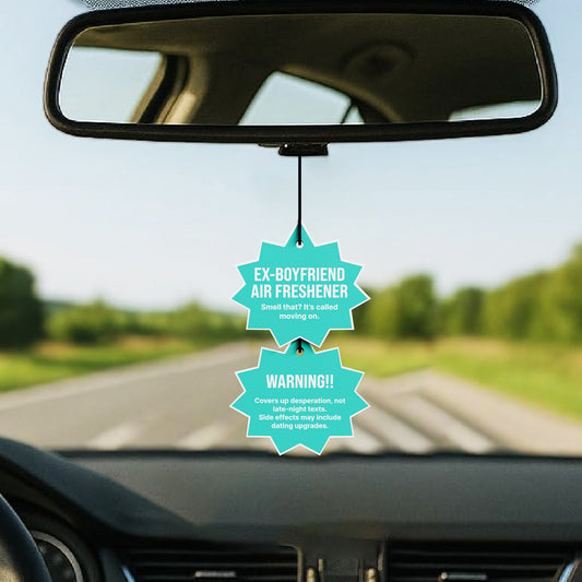 Car air freshener with humorous label hanging from a car's rearview mirror.