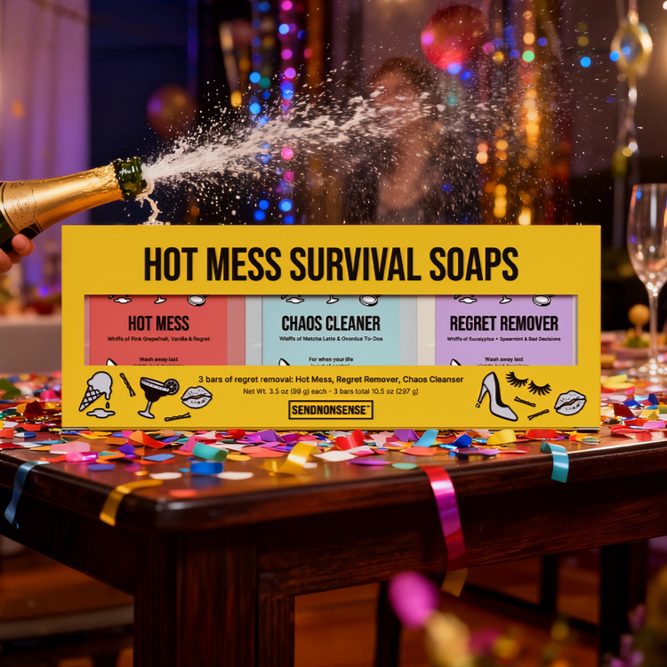 Box of 'Hot Mess Survival Soaps' with champagne being poured over it on a celebratory table.